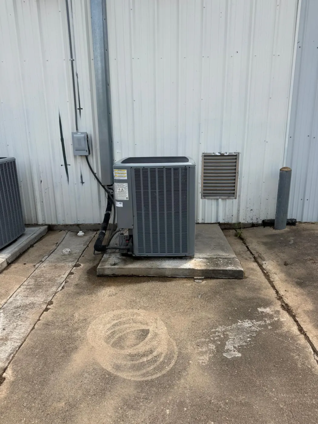The same concrete pad beside the building, with a new clean condenser unit installed and the ground cleared