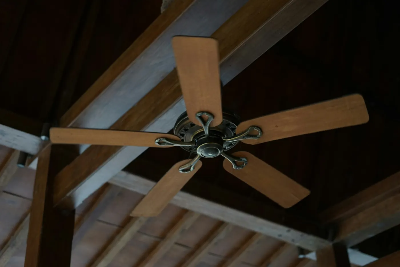 A five-blade wooden ceiling fan mounted under exposed beams